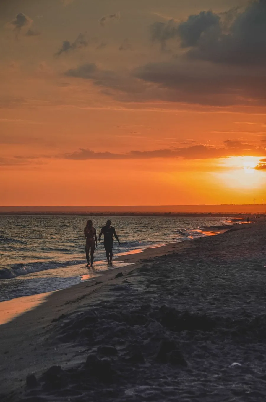 A couple walking along the shoreline at sunset